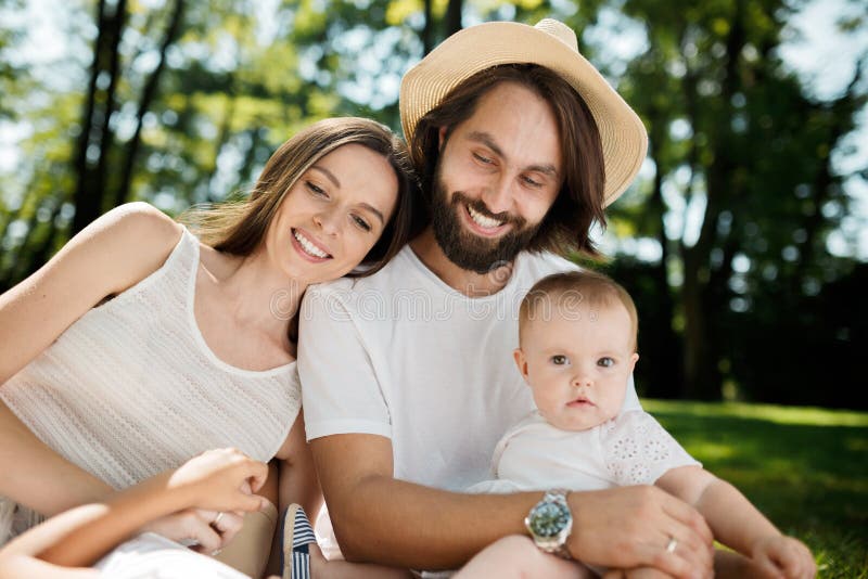 Young dark-haired mother and father dressed in white clothes are holding in the arms little charming daughter and stock photos Young dark-haired mother and father dressed in white clothes are holding in the arms little charming daughter and stock photos