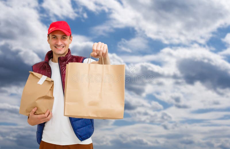 Young Delivery Man Carrying Cardboard Box in Front of Sky Background