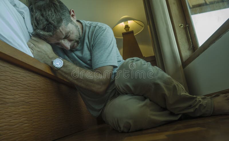 Young depressed and desperate man sitting on bedroom floor next to bed suffering depression and anxiety feeling overwhelmed and stock images Young depressed and desperate man sitting on bedroom floor next to bed suffering depression and anxiety feeling overwhelmed and stock images