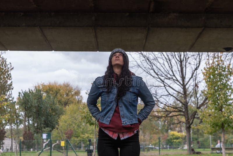 Young depressed homeless girl or woman standing alone under the bridge on the street on the cold weather feeling anxious abandoned and freezing selective focus