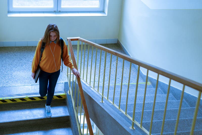 Young depressed lonely female college student walking down the stairs at her school, looking down.