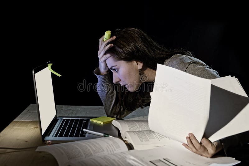 Young desperate university student girl in stress for exam studying with books and computer laptop late at night