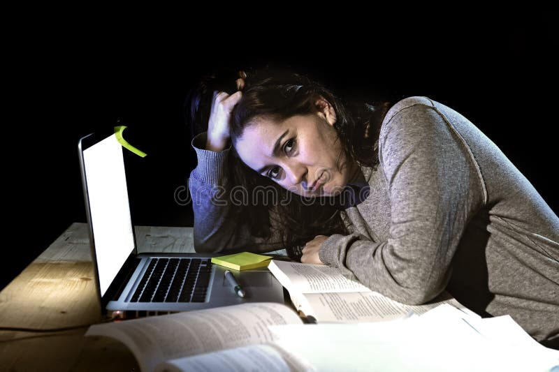 Young desperate university student girl in stress for exam studying with books and computer laptop late at night