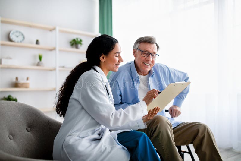 Young doctor asking senior impaired male patient in wheelchair to sign insurance policy at home royalty free stock image Young doctor asking senior impaired male patient in wheelchair to sign insurance policy at home royalty free stock image