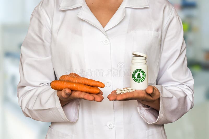 Young doctor holding carrots and bottle of pills with vitamin A stock photography Young doctor holding carrots and bottle of pills with vitamin A stock photography