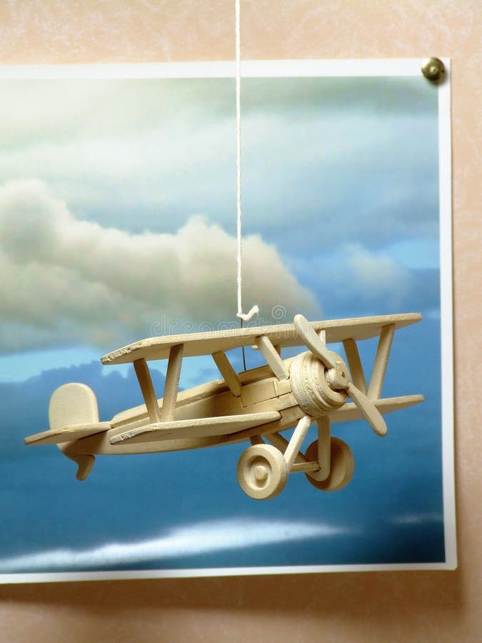 A simple wooden model of a World War One fighter plane - hanging on a string in front of a photograph of clouds. A simple wooden model of a World War One fighter plane - hanging on a string in front of a photograph of clouds.