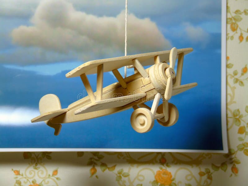 A simple wooden model of a World War One fighter plane - hanging on a string in front of a photograph of clouds. A simple wooden model of a World War One fighter plane - hanging on a string in front of a photograph of clouds.