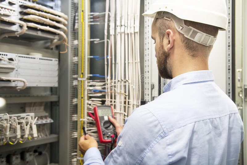 Young electrician working on electric panel. Electrician engineer tests electrical installations and wires on relay protection stock photo