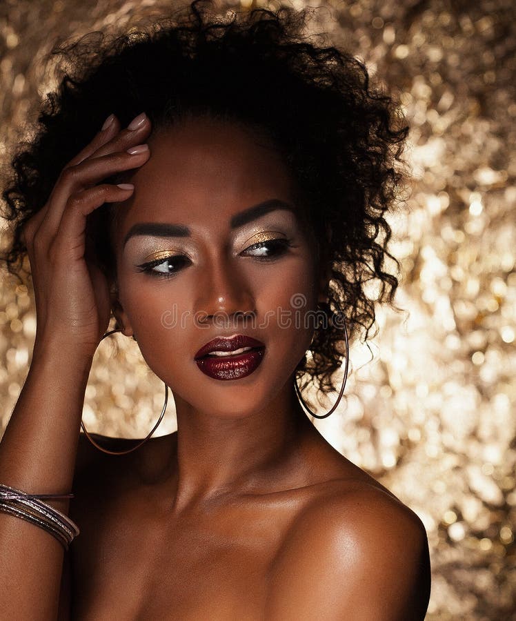 Young elegant african american woman with afro hair. Glamour makeup. Golden Background.