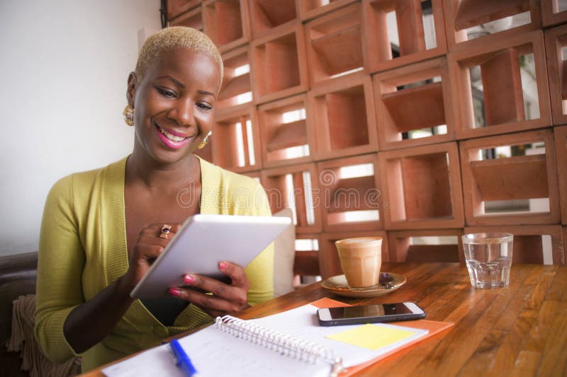 Young elegant and beautiful black African American business woman working online with digital tablet pad at coffee shop smiling ha