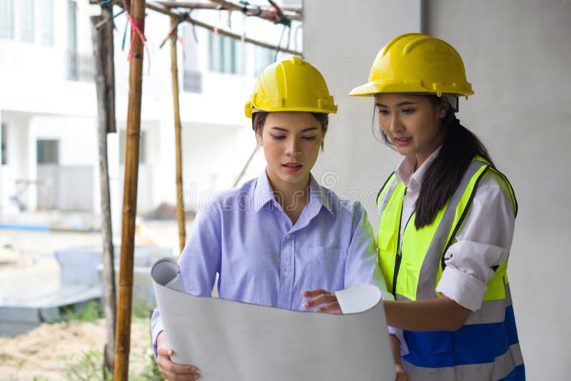 Young engineer in a construction helmet and safety vest explaining to project owner about a floor plan. Work environment of royalty free stock images