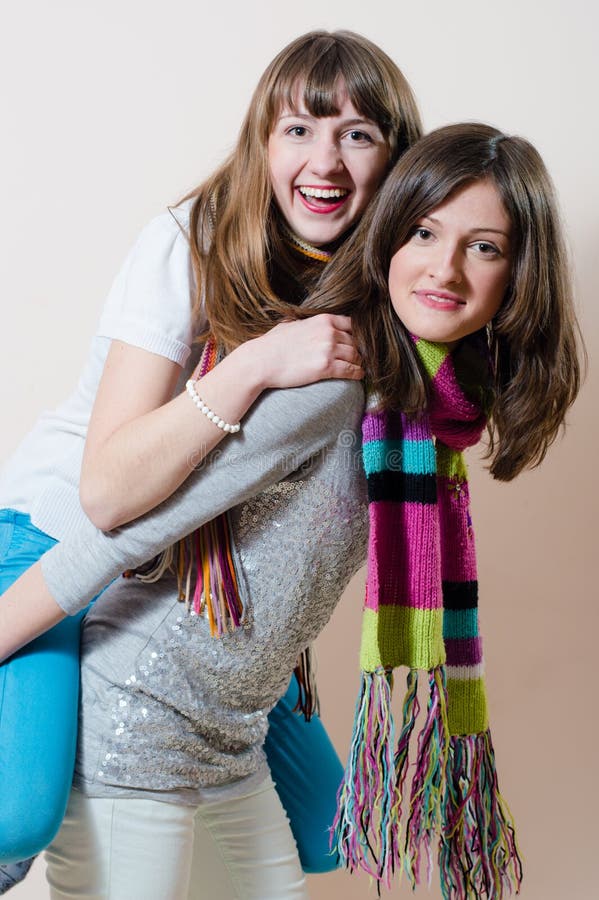 2 young enjoyable pretty women having fun friendly hugging and riding happy smiling & looking at camera