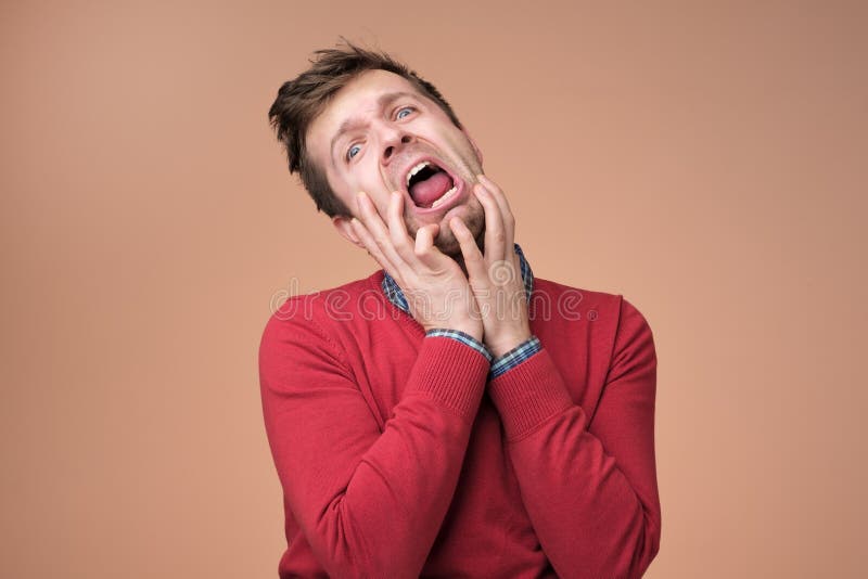 Young european man in red sweater crying of pain anf grief on brown background. royalty free stock image Young european man in red sweater crying of pain anf grief on brown background. royalty free stock image