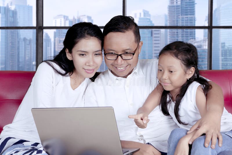 Young family using a laptop computer while sitting together on the sofa. Shot in the apartment. Young family using a laptop computer while sitting together on the sofa. Shot in the apartment