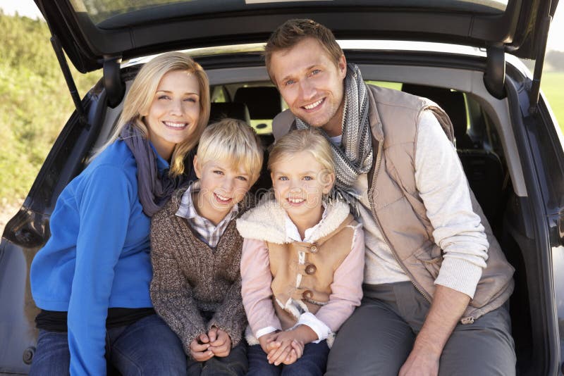 Young family pose together at rear of car smiling