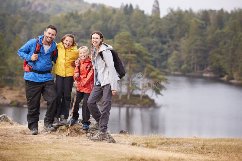 Young family standing on a rock by a lake looking to camera embracing, full length stock photography Young family standing on a rock by a lake looking to camera embracing, full length stock photography