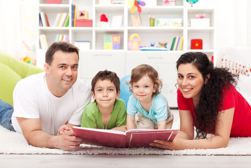 Giovane famiglia felice con due bambini, la lettura di un libro di storia posa sul pavimento.