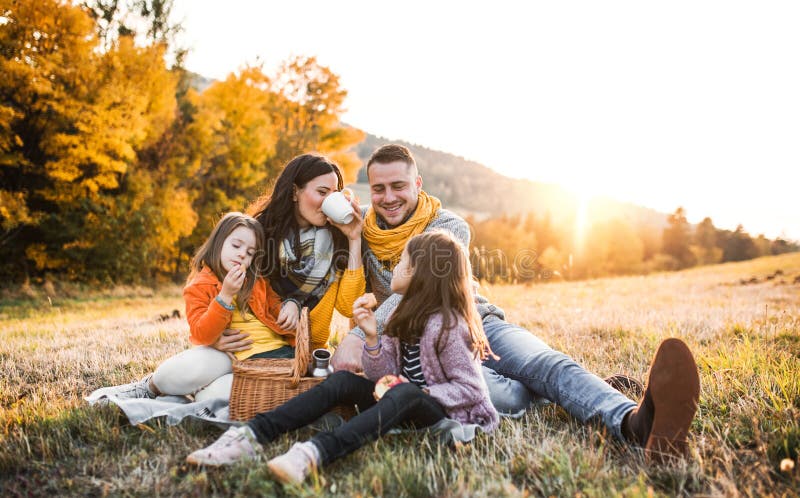 A portrait of happy young family with two small children sitting on a ground in autumn nature at sunset, having picnic. A portrait of happy young family with two small children sitting on a ground in autumn nature at sunset, having picnic.