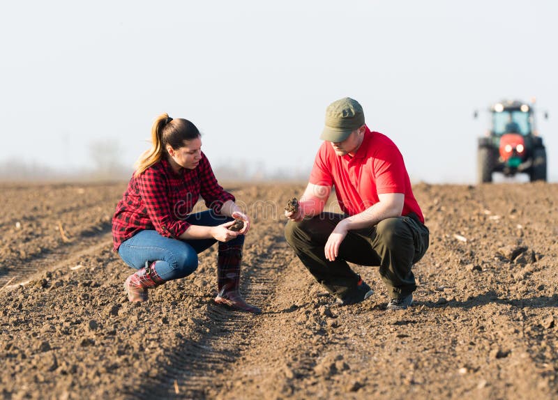 Young farmers examing dirt while tractor is plowing fields