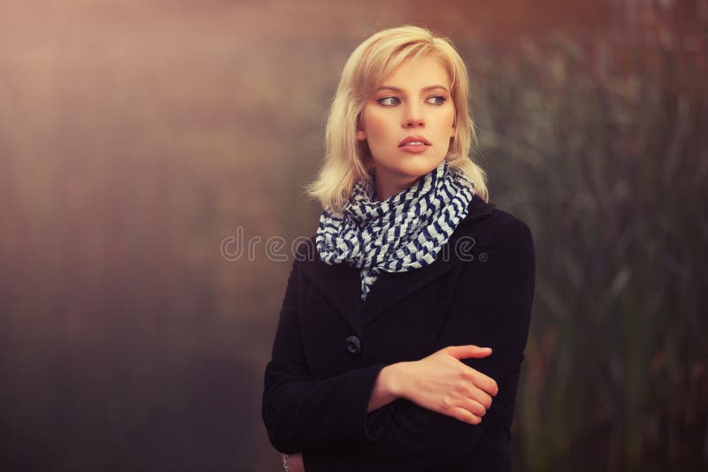 Young fashion blond woman in black coat walking in a fog outdoor