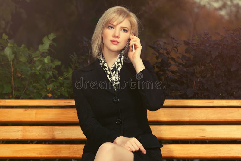 Young fashion blond woman talking on mobile phone in city park