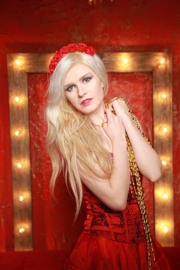 Young fashion blonde lady posing in red corset dress on red fashion background with lamp bulbs frame with yellow warm royalty free stock photo Young fashion blonde lady posing in red corset dress on red fashion background with lamp bulbs frame with yellow warm royalty free stock photo