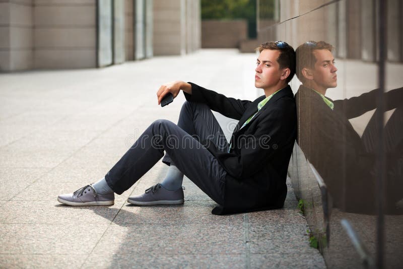 Young fashion business man with smartphone sitting at the wall