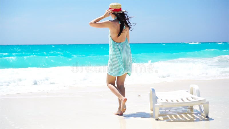 Young beautiful woman on white sand tropical beach. Back view of caucasian girl in hat background the sea
