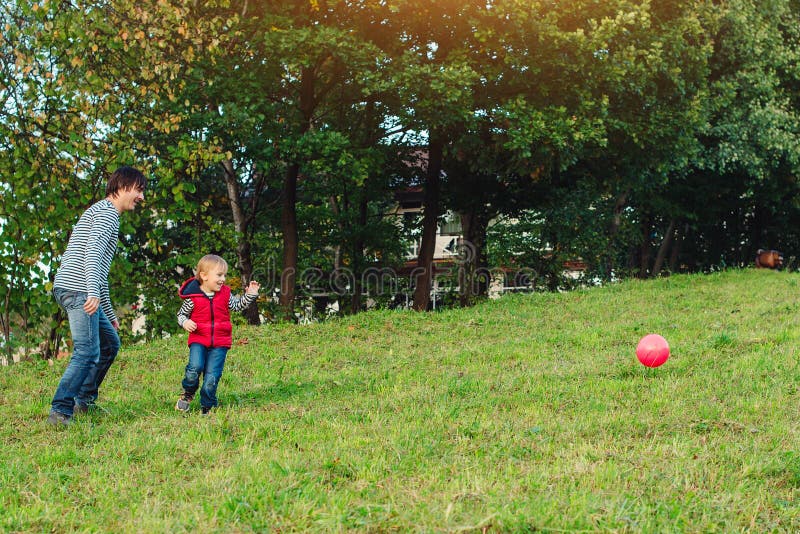 Young father with his little son playing football on green grassy lawn.