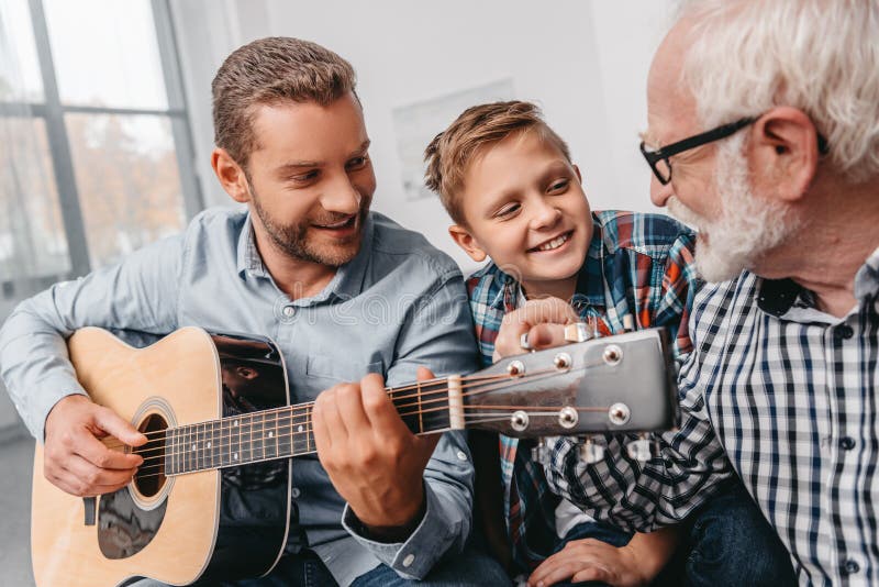 Young father playing guitar while little son and grandfather are royalty free stock images Young father playing guitar while little son and grandfather are royalty free stock images