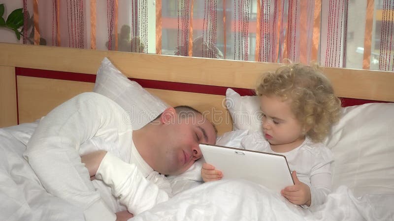 young father sleep in bed and daughter nearby play with tablet. childhood. 4K