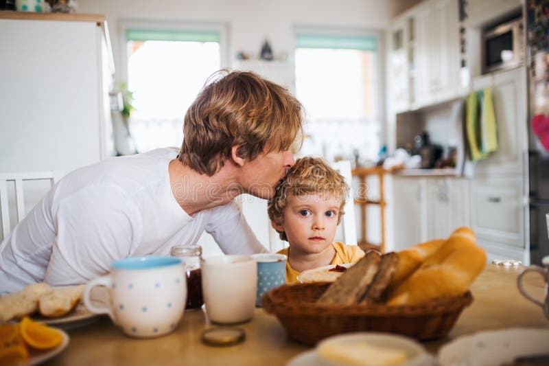 Young father with a toddler son eating breakfast indoors at home. stock photography Young father with a toddler son eating breakfast indoors at home. stock photography
