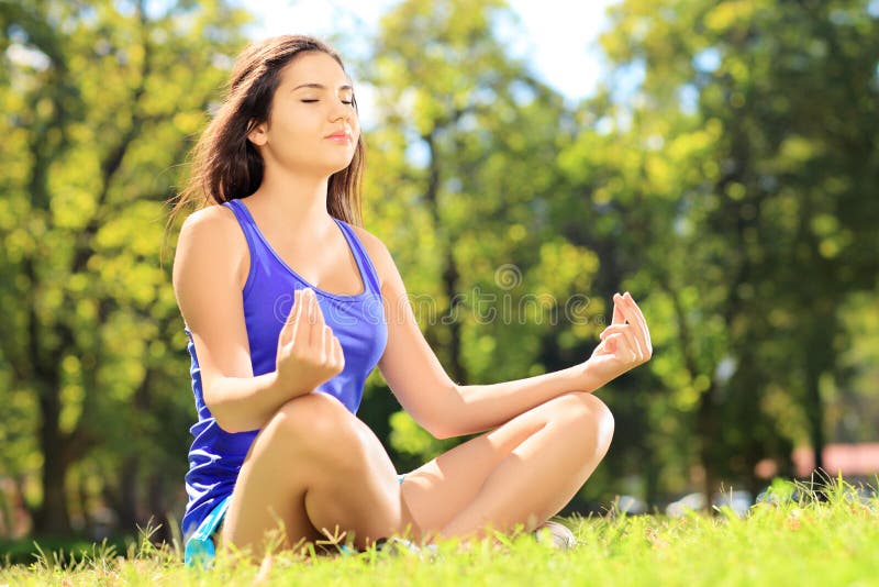 Young female athlete in sportswear meditating seated on a grass. Young female athlete in sportswear meditating seated on a green grass in a park stock photos Young female athlete in sportswear meditating seated on a grass. Young female athlete in sportswear meditating seated on a green grass in a park stock photos