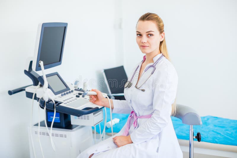Young female blonde doctor with stethoscope on her neck siting near ultrasound machine stock photography Young female blonde doctor with stethoscope on her neck siting near ultrasound machine stock photography