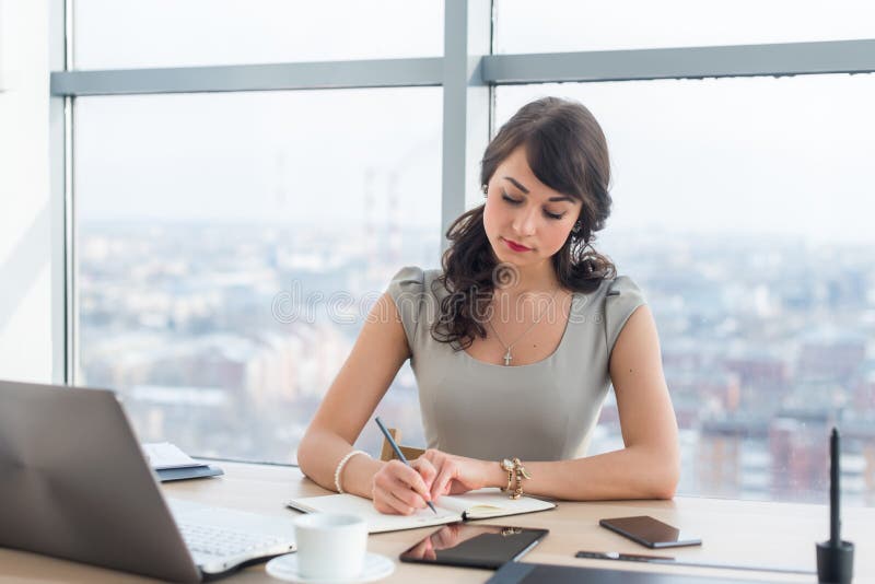 Young Female Clerk Sitting at Modern Office Making Notes in Her Notepad