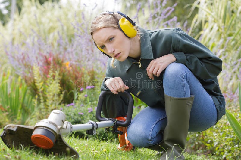 young female gardener crouching down to examine strimmer