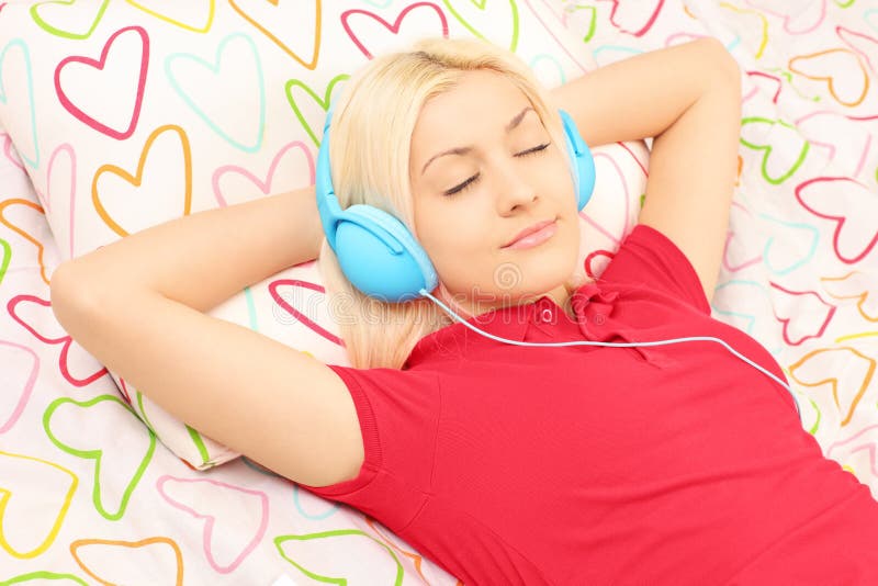 Young female lying on a bed and listening music