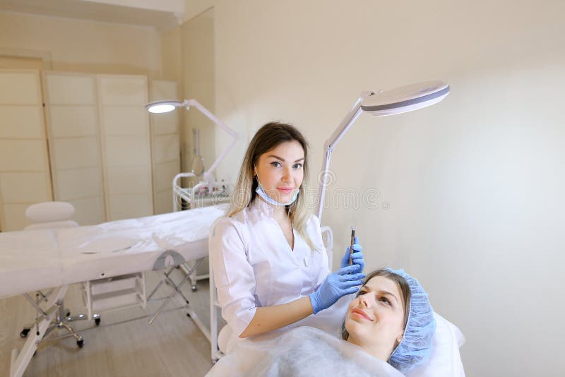 Young woman getting makeup by eyebrow tattoo pen by cosmetologist. stock photography Young woman getting makeup by eyebrow tattoo pen by cosmetologist. stock photography
