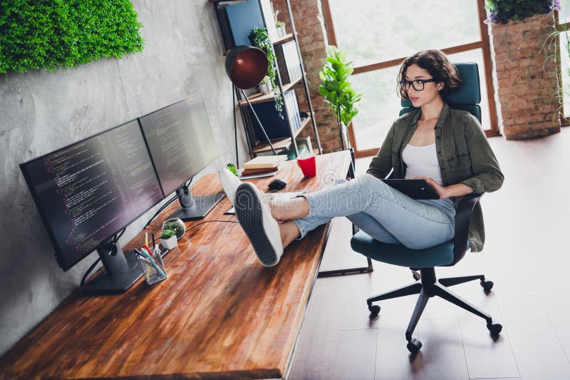Young female programmer working casually at a modern workspace, coding on dual monitors while relaxing and enjoying the royalty free stock image