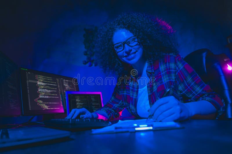 Young female programmer working on code in a dimly lit workspace, surrounded by multiple screens royalty free stock images