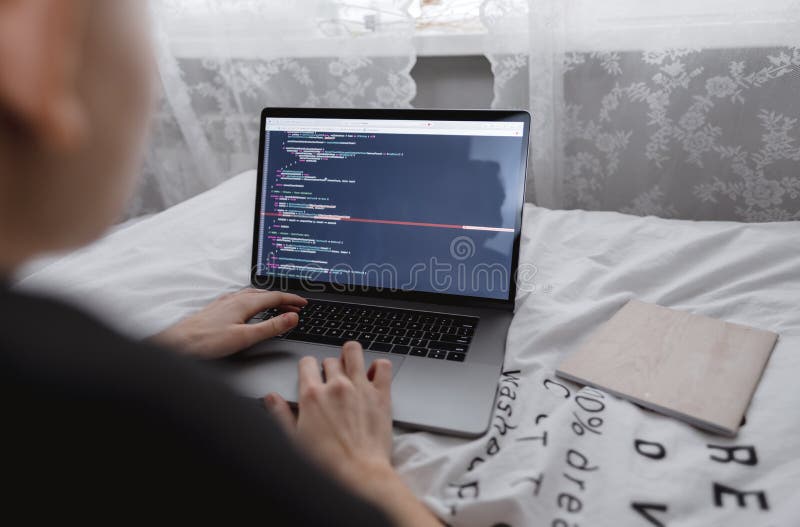 Young female programmer writes program code on a computer laptop in the bed. remote work. High quality photo.
