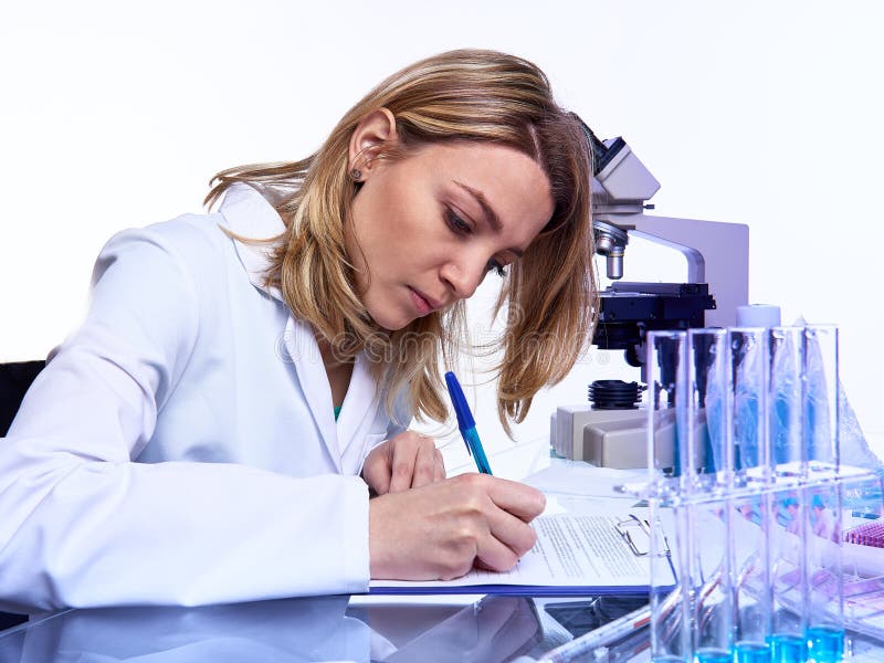 Young female scientist or tech writes report or lab journal in modern laboratory with microscope  glass tubes with samples and