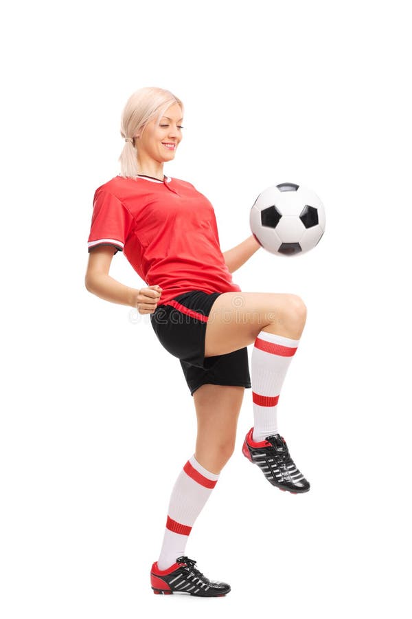 Full length portrait of a young female soccer player in a red jersey and black shorts juggling a football isolated on white background. Full length portrait of a young female soccer player in a red jersey and black shorts juggling a football isolated on white background