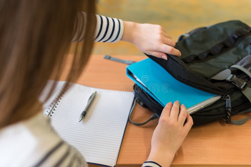 Young female student behind her desk at class, taking out her textbooks.