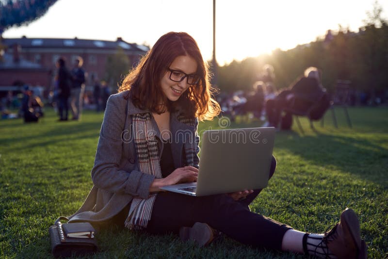 Young female student doing homework on laptop sitting on green grass in the Park. Red long hair and glasses. Concept training, bus stock photos Young female student doing homework on laptop sitting on green grass in the Park. Red long hair and glasses. Concept training, bus stock photos