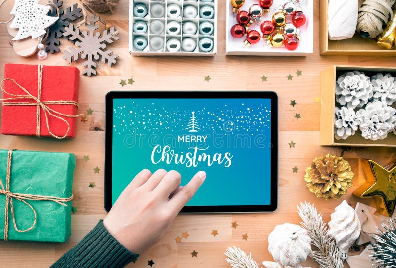 Young female using tablet with merry christmas text sign on screen and ornament element for decorating on wood tabl stock photos
