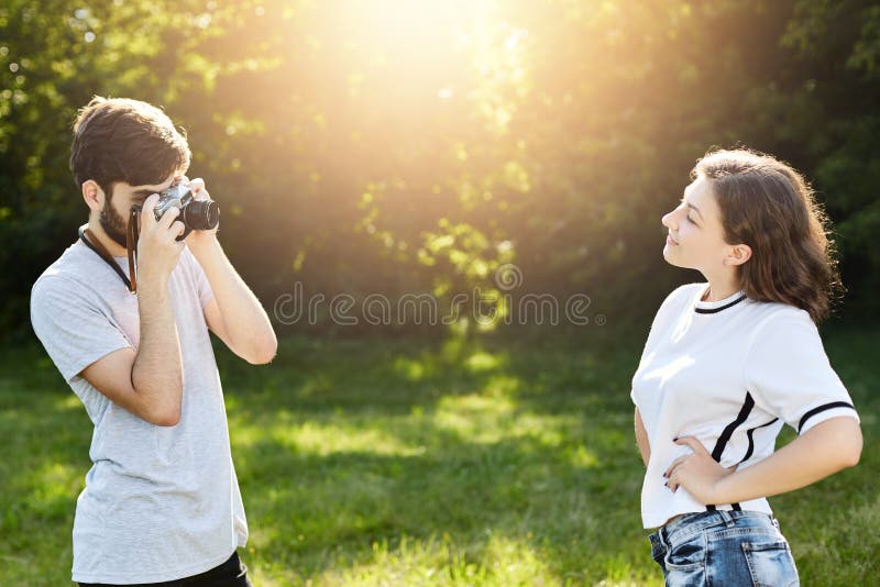 Young female wearing T-shirt and jeans posing in camera to photographer. Young talented male with retro camera photographing prett stock photography Young female wearing T-shirt and jeans posing in camera to photographer. Young talented male with retro camera photographing prett stock photography