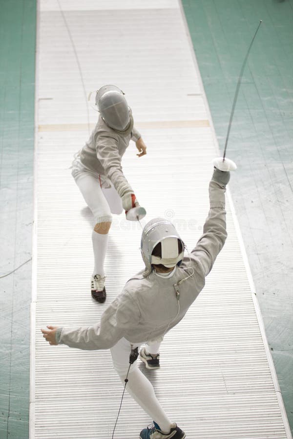 Young fencers in protective costumes fighting on the fencing competition stock photo Young fencers in protective costumes fighting on the fencing competition stock photo