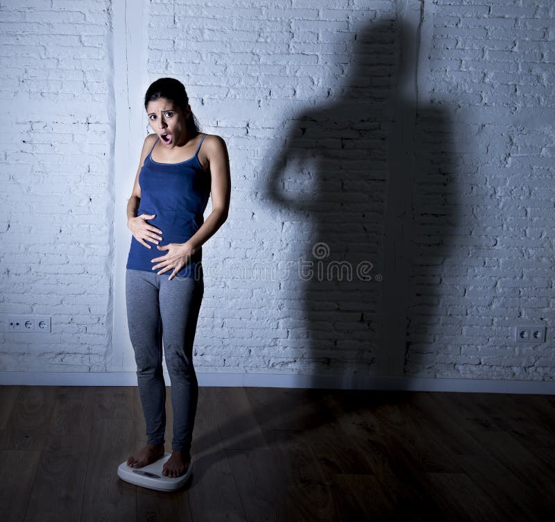 Young fit and slim woman checking body weight on scale with big edgy shadow light sad and desperate