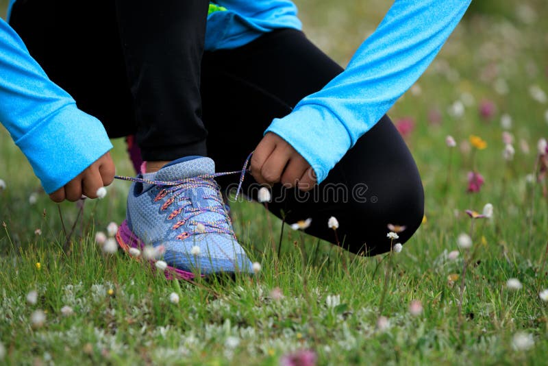 Fitness woman runner tying shoelace on grassland